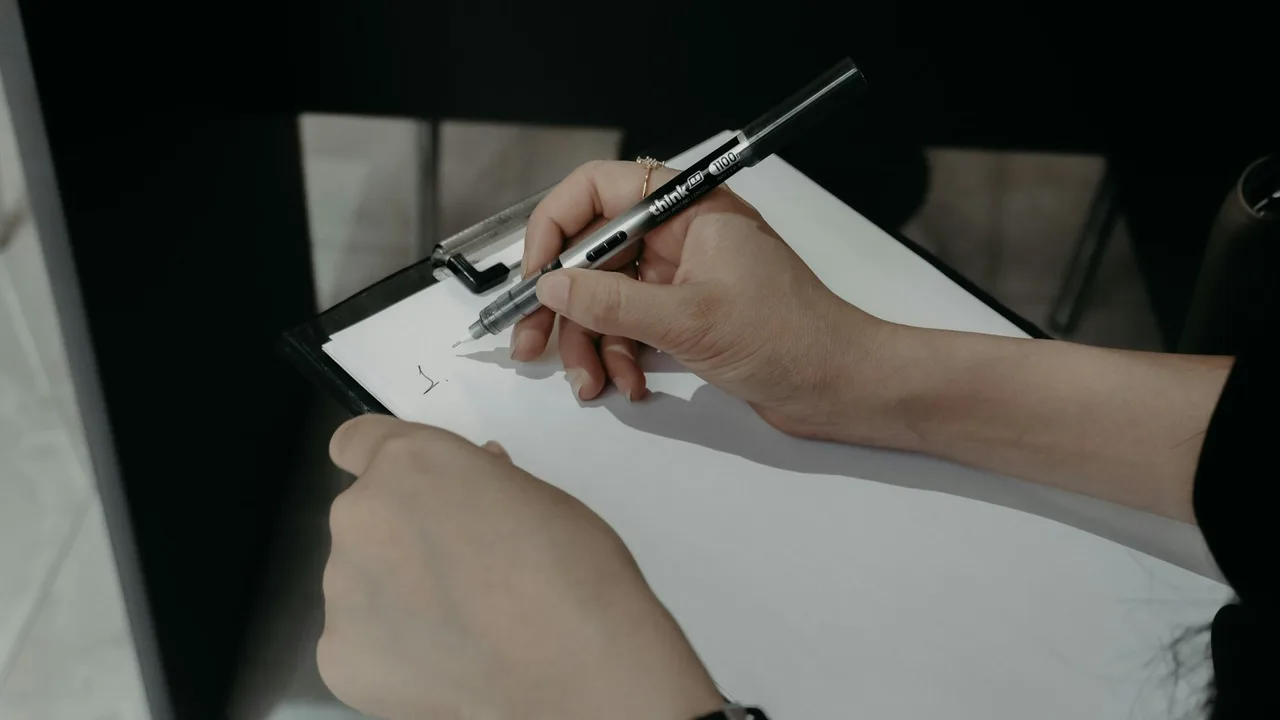 Hands writing notes on a clipboard with a pen Hands writing notes on a clipboard with a pen