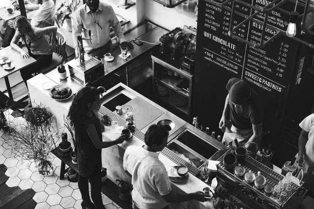Cafe counter seen from above, with staff serving and chalkboard menus overhead