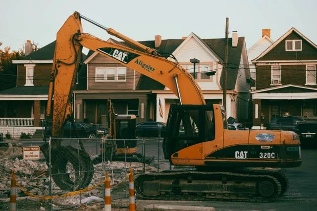 Excavator clearing a demolition site beside established weatherboard homes