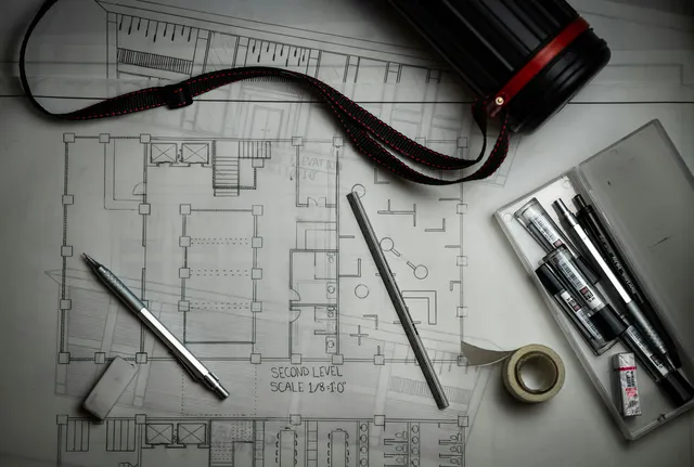 Architectural house plans laid flat with drafting pencils and a metal ruler