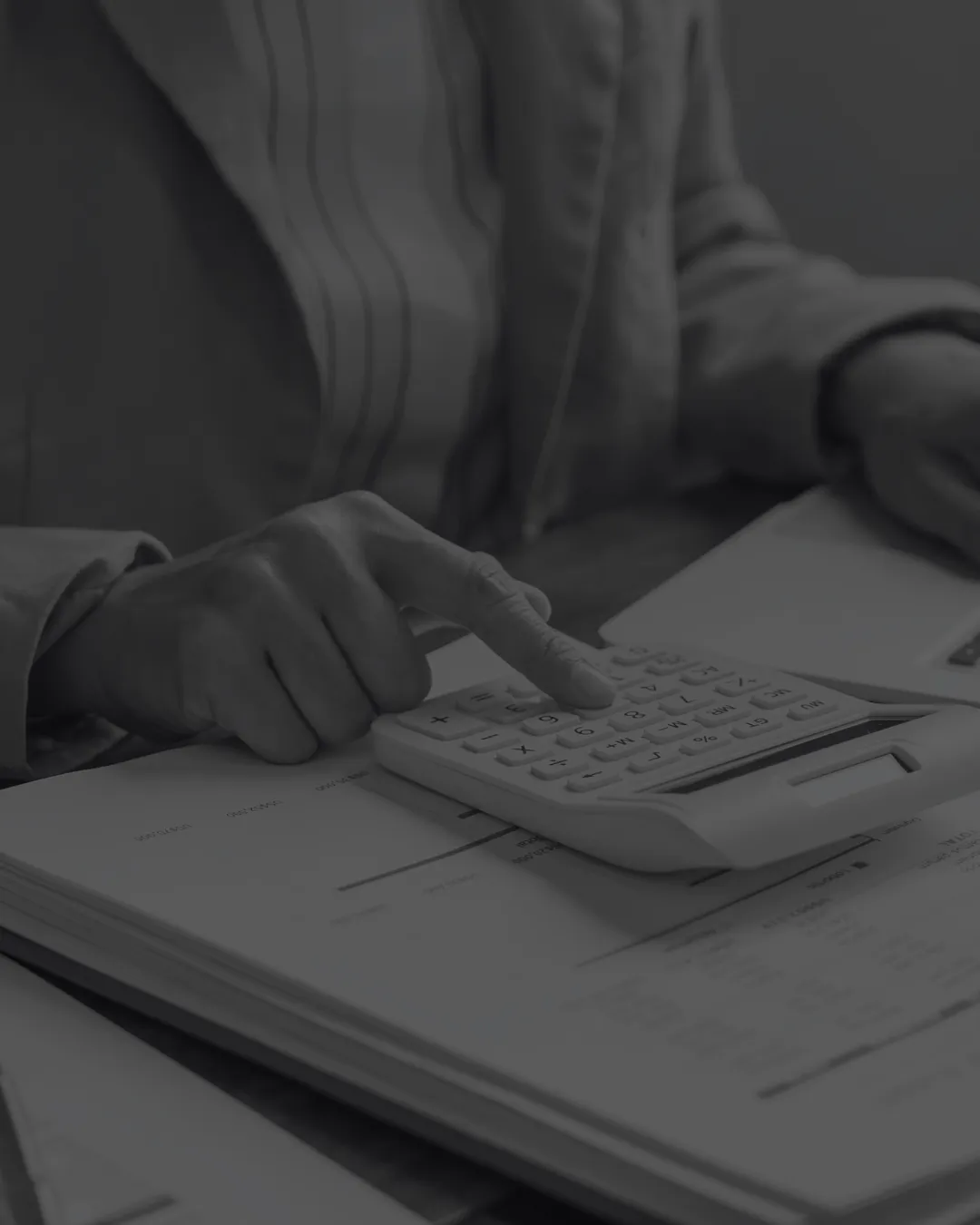 Person using a calculator over stacks of printed financial statements
