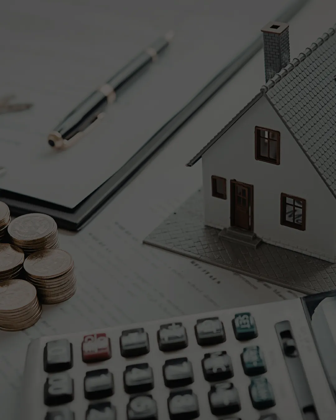 Model house beside stacked coins, a calculator and paperwork on a desk