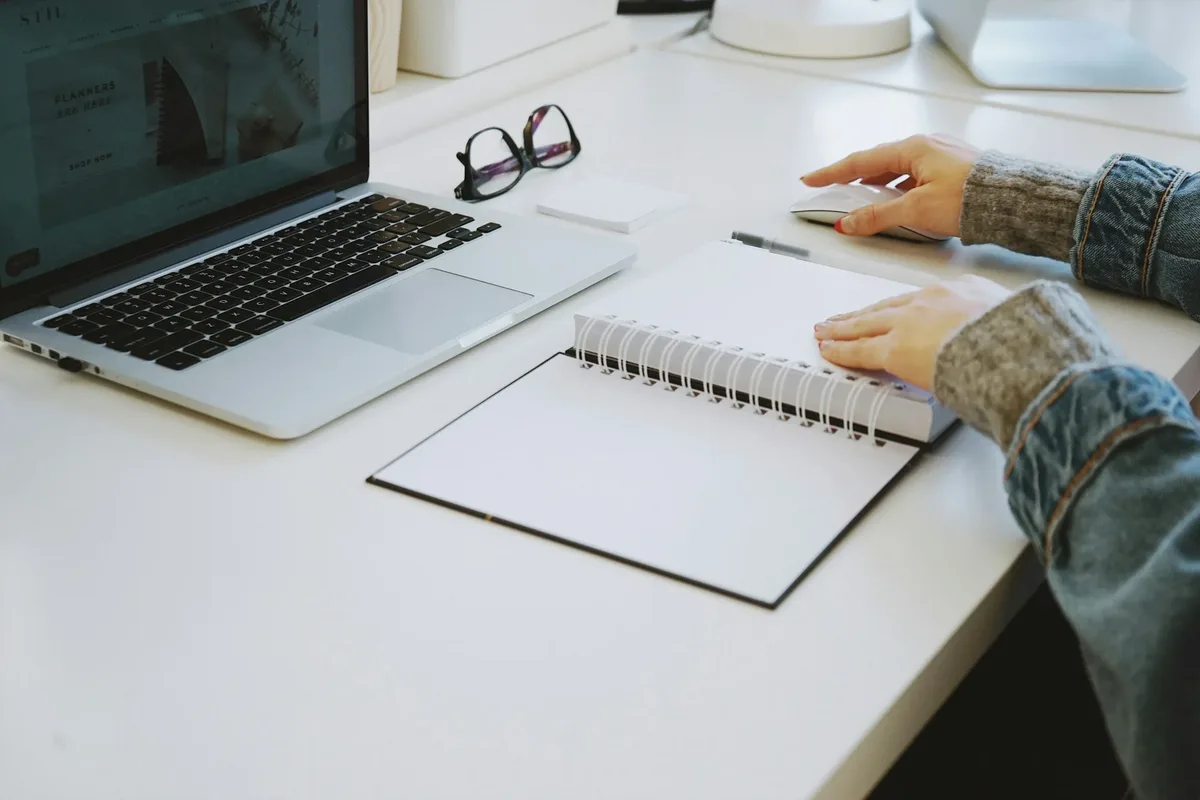 Hands at a desk with a laptop and a spiral notebook Hands at a desk with a laptop and a spiral notebook