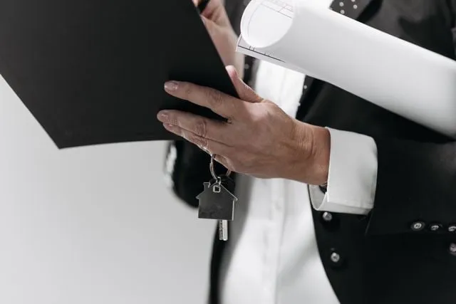 Person in business attire holding house keys and a property blueprint