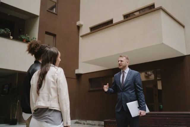A professional in a suit discussing a residential building with two people during a site visit
