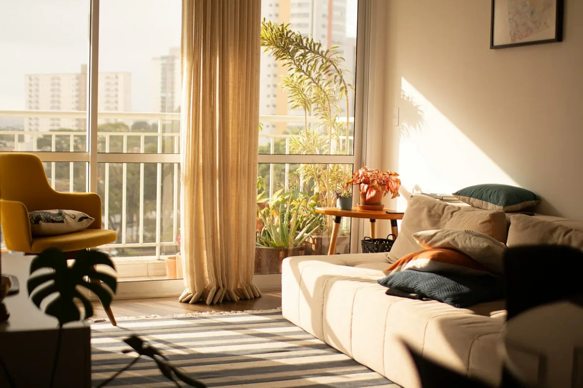 Sunlit apartment living room with a sofa, curtains and floor-to-ceiling windows Sunlit apartment living room with a sofa, curtains and floor-to-ceiling windows